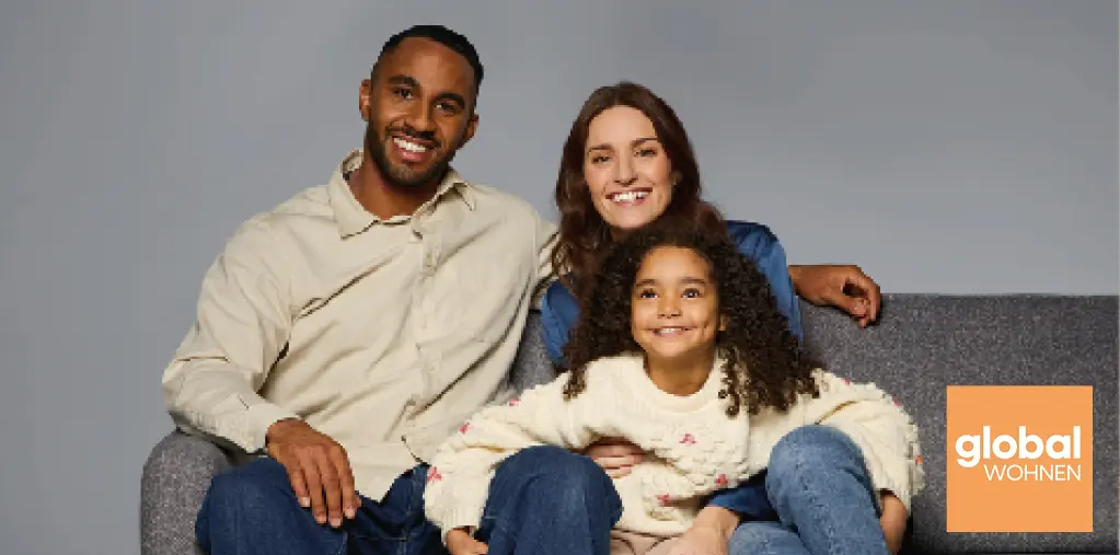 Glückliche Familie sitzt auf grauem Sofa im modernen Wohnzimmer-Stil. Eltern und Kind posieren entspannt für Wohnmöbel-Kampagne von global wohnen. Gemütliche Couch in zeitlosem Design für Familien und Wohnkomfort.